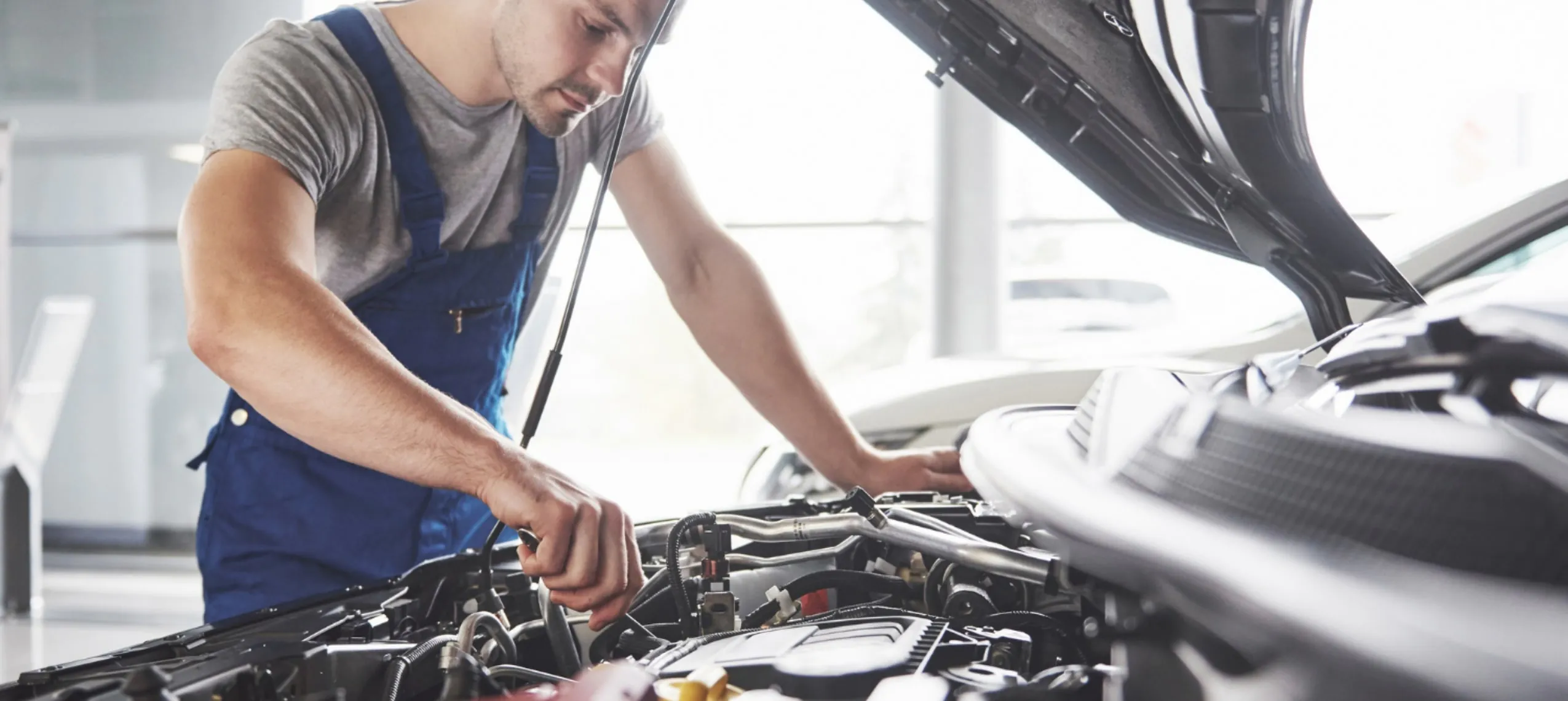 Revisión pre-compra de un coche de segunda mano: mecánico con mono azul revisando el motor con el capó abierto